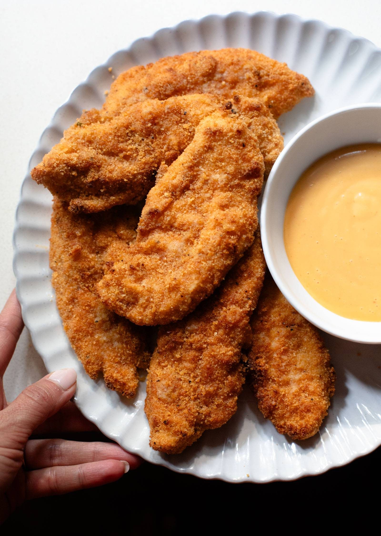 Chicken tenders on a plate with sauce on the side.