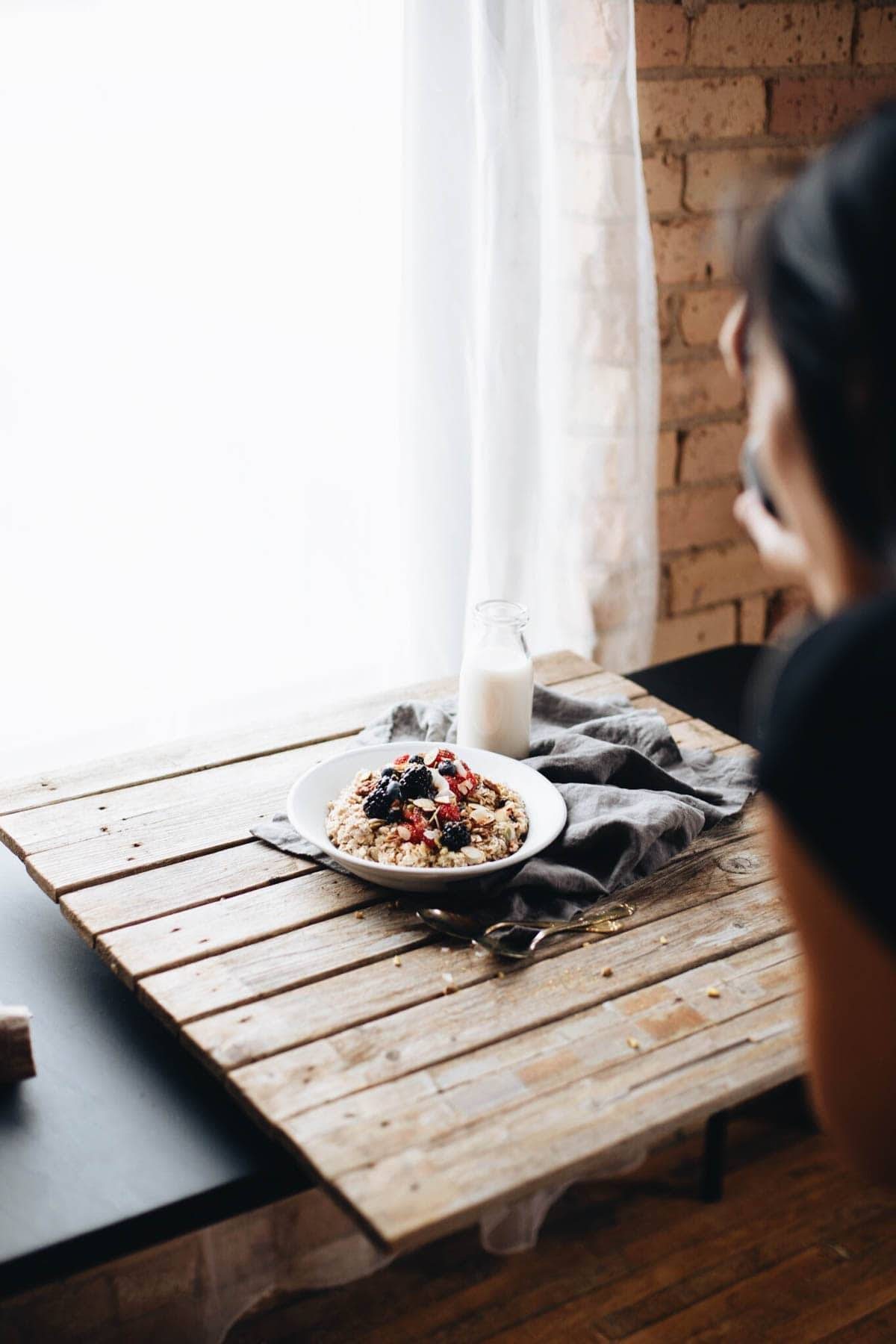 A bowl of granola and berries with a glass of milk on a wood slab.