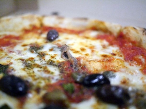 close up of tomato, garlic, oregano, capers, olives, anchovies & mozzarella pizza from franco manca